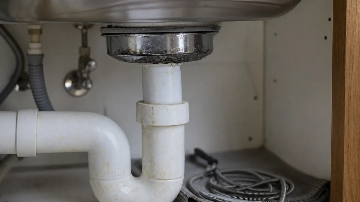 Fachmann führt eine Rohrreinigungsspirale in den Küchenabfluss unter der Spüle ein